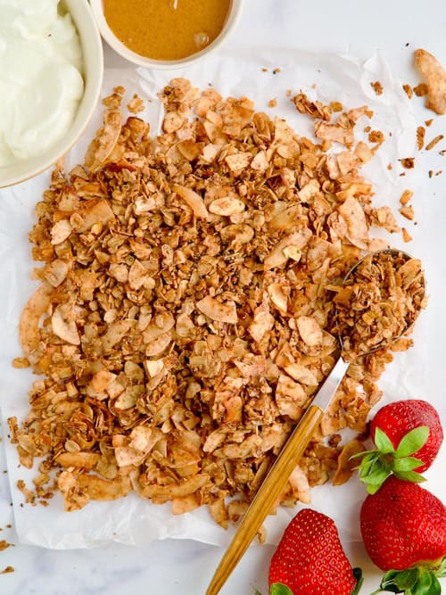 Sugar free granola on parchment paper next to yogurt and strawberries. Sugar free granola on parchment paper next to yogurt and strawberries.