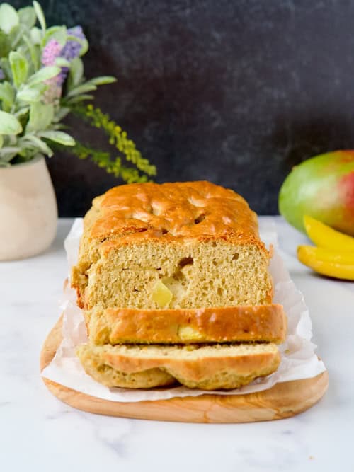 Sugar-free mango & banana bread on a wooden board with 3 slices cut.