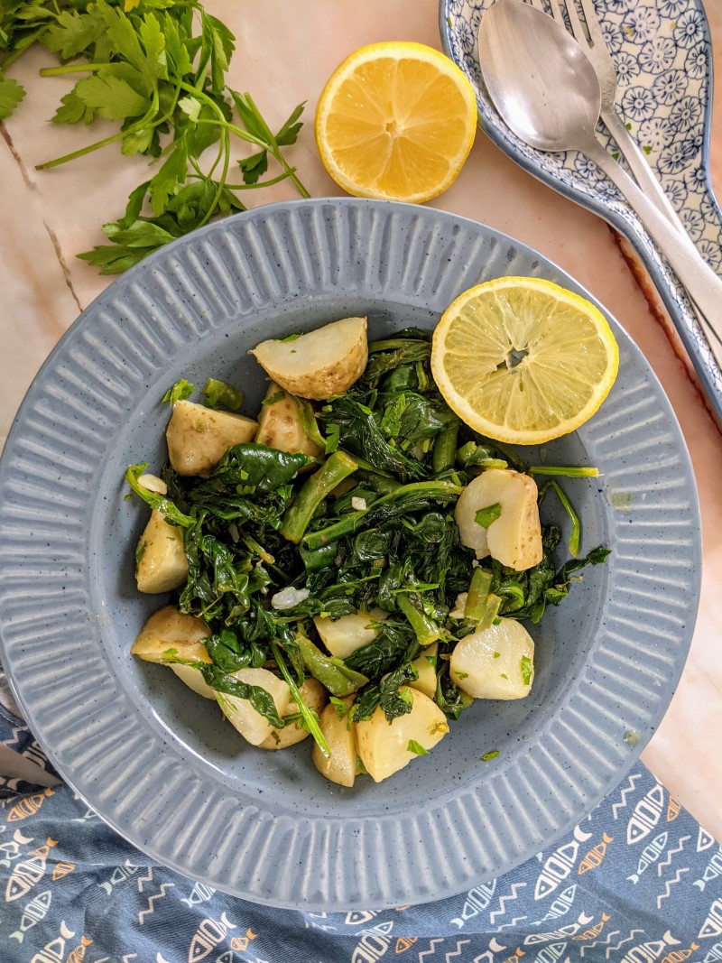 Swiss Chard & Potato Salad served on blue plate next to slices of lemon