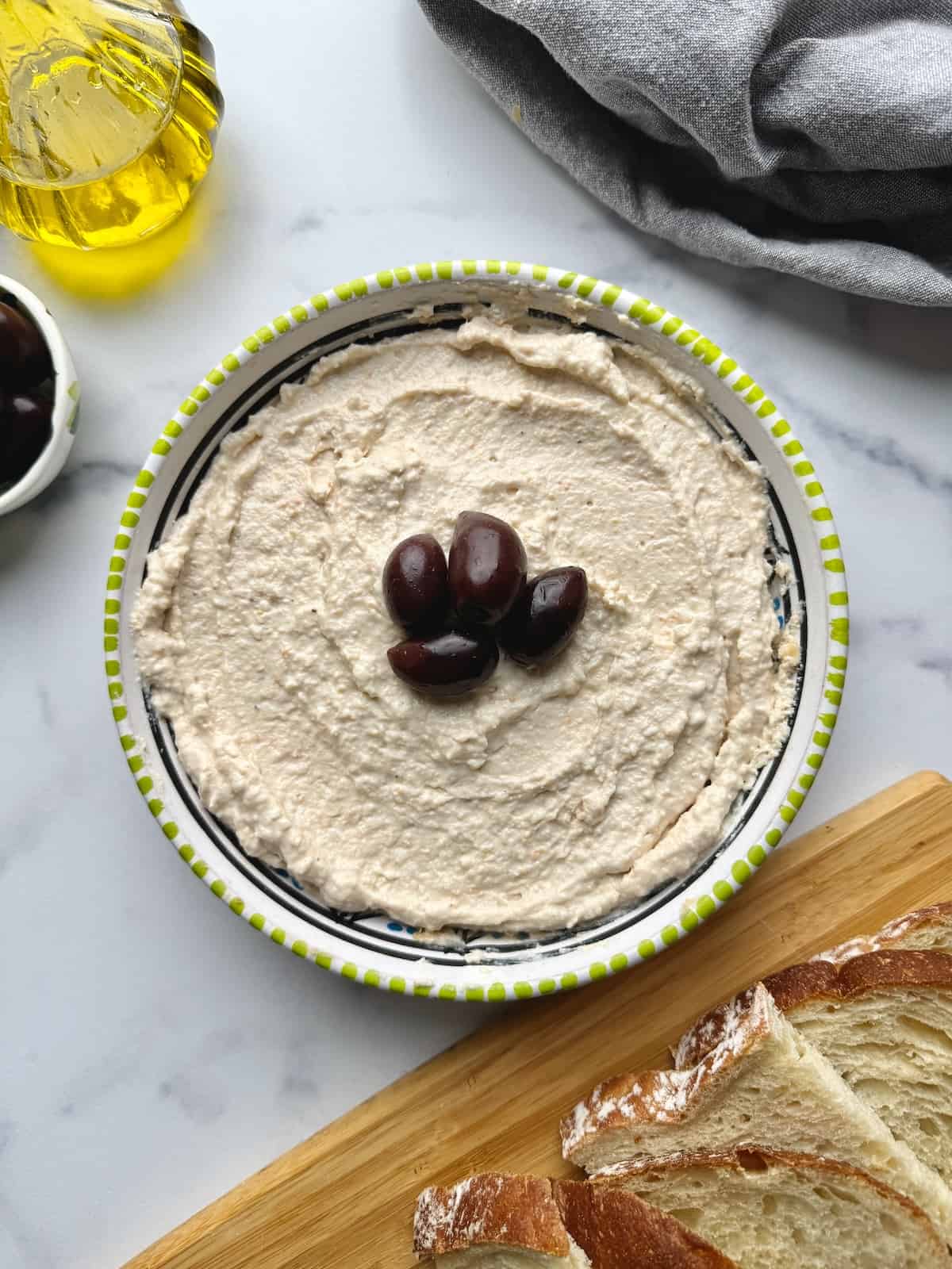 Taramasalata served on plate with olives, next to bread slices and olive oil.