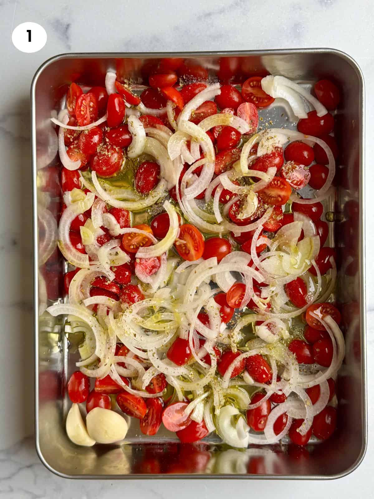 Tomatoes and onion slices in the tray ready to be roasted.