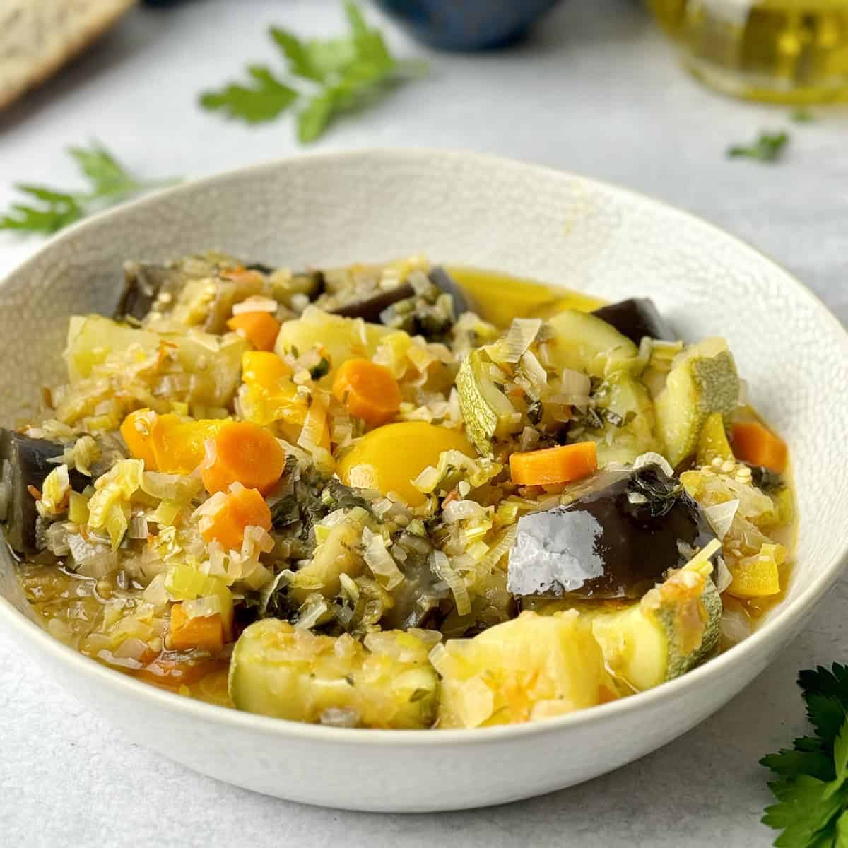 White bowl with tourlou vegetable stew and olive oil bottle in the background.