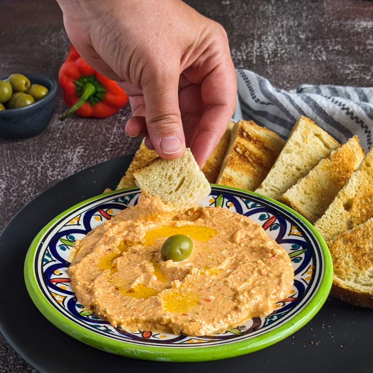 Greek spicy feta cheese dip served on a plate with an olive on top and next to slices of bread.