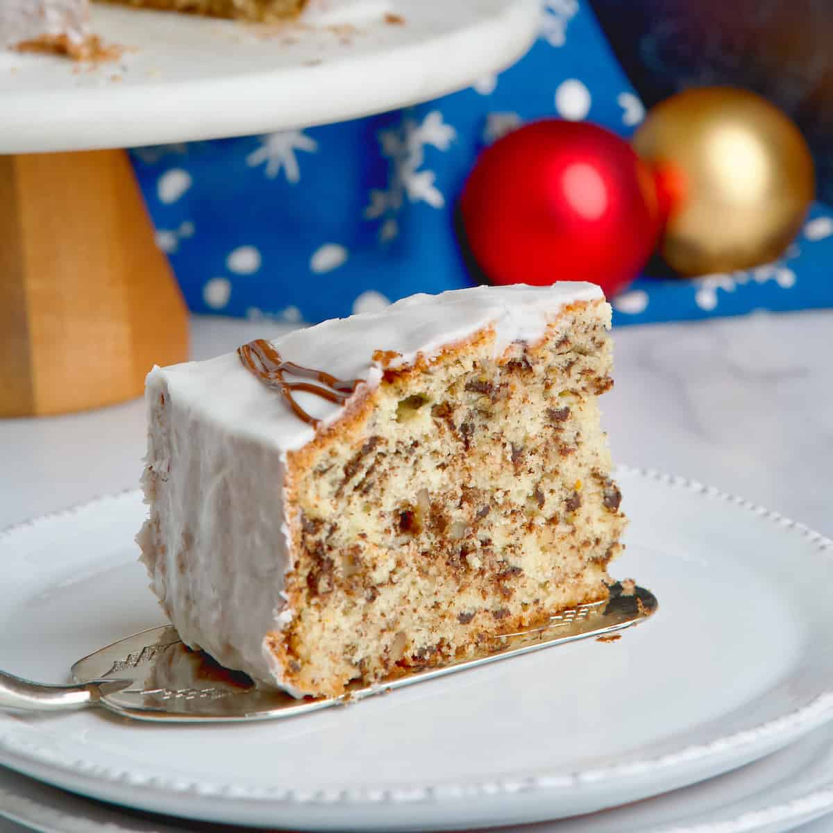 Vasilopita cake slice served on white plate with the whole cake in the background on a cake stand.