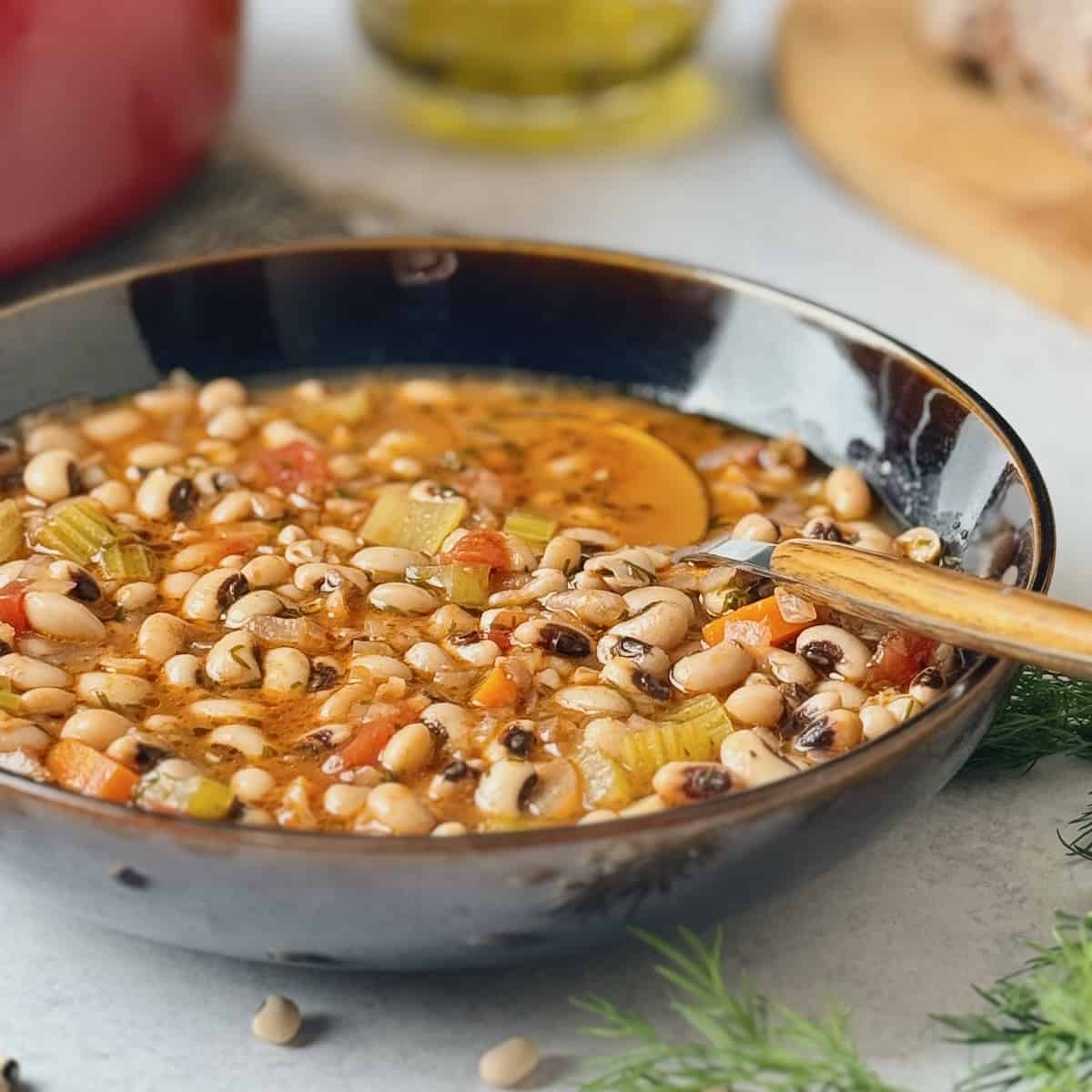 Greek black eyed peas soup served on black bowl next to bread and a bottle with olive oil in.