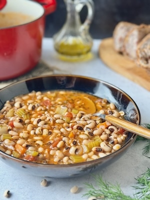 Greek black eyed peas soup served on black bowl next to bread and a bottle with olive oil in.