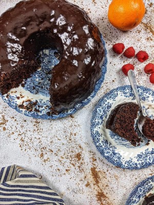 Κέικ σοκολάτας και δίπλα πιάτο με μερίδα κέικ σερβιρισμένο και raspberries δίπλα