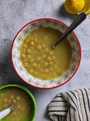 Lemony Greek chickpea soup served in a bowl with a slice of lemon on the side.