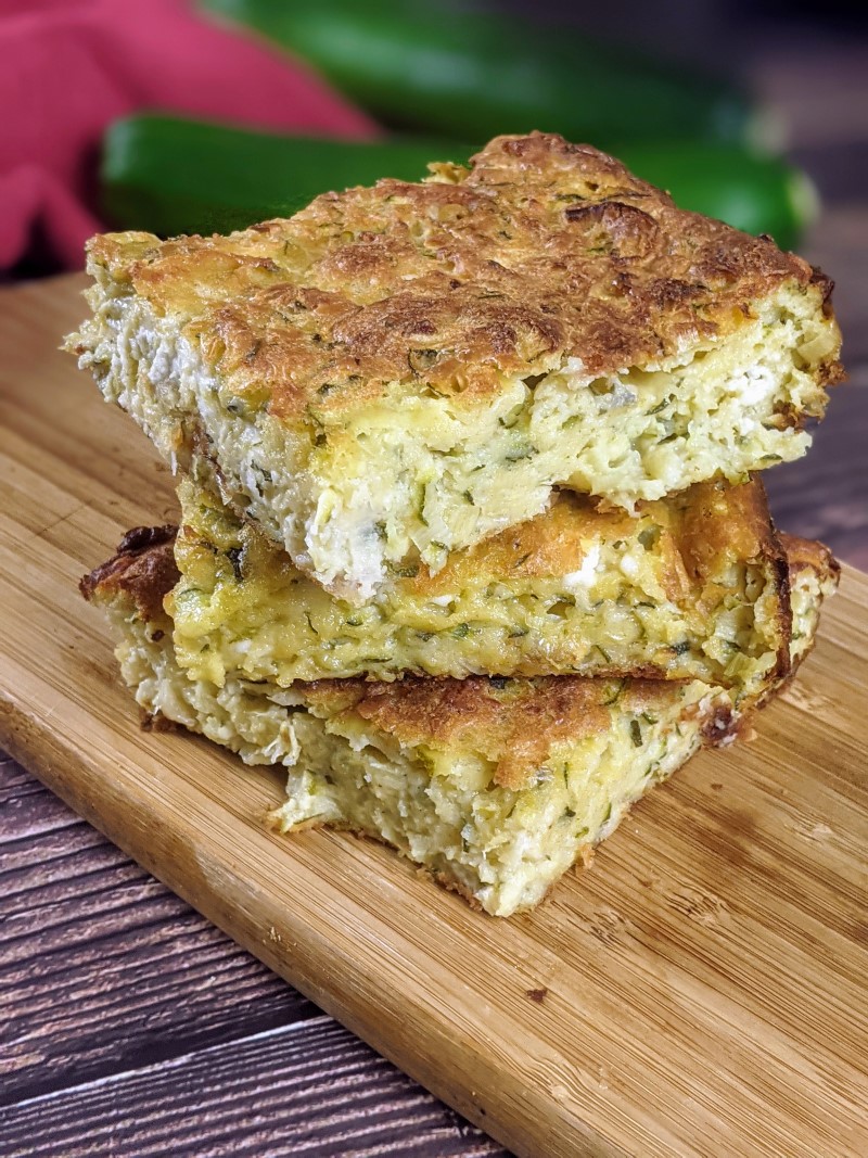 Three slices of zucchini pie stack on top of each other on top of wooden board