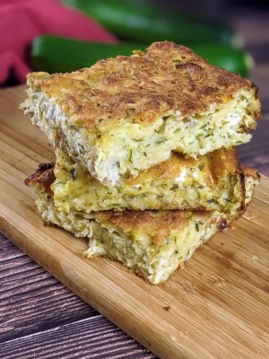 Three slices of crustless zucchini pie stack on top of each other on a wooden board.